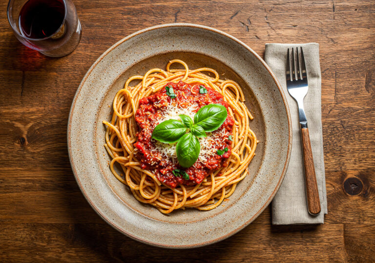 Spaghetti mit Tomatensauce, veganem Hack und Basilikumblättern auf Holztisch, Draufsicht, KI-generiert