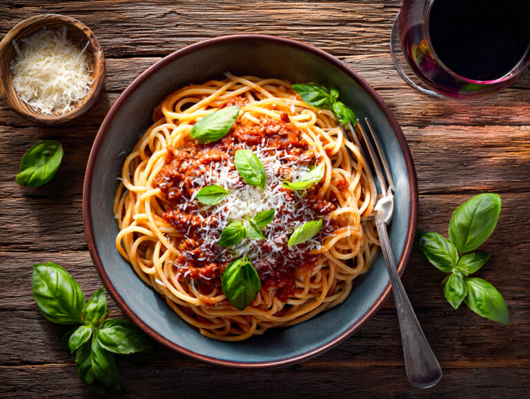 Italienische Spaghetti mit veganem Hack, Tomatensauce, Basilikum und Parmesan auf Holztisch, KI-generiert