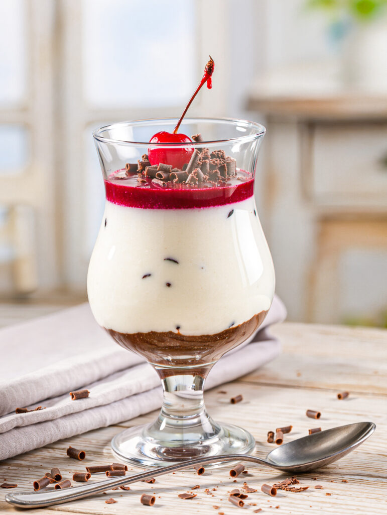 Vanilledessert im Glas mit roter Kirschsoße und Schokoraspeln, KI-generiert